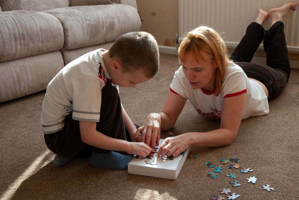 Mother and child working on a puzzle while sitting on a clean carpet in a living room, sunlight streaming through the window.