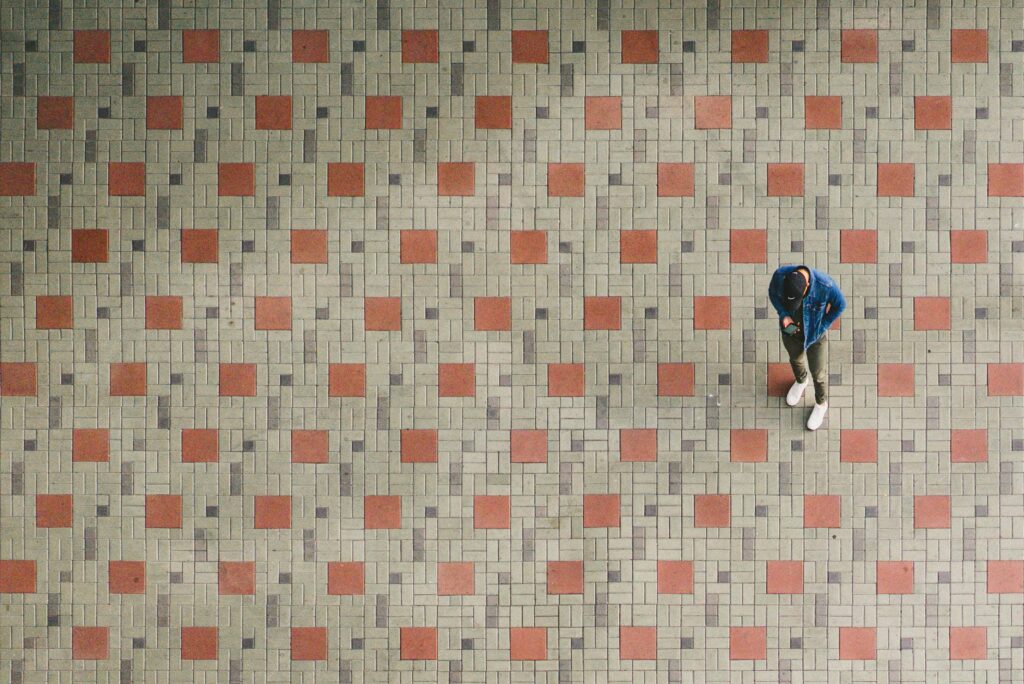 A person walking across a patterned tiled floor, showing a mix of red and gray square tiles, perfect for discussing tile cleaning techniques in Manhattan Beach, CA.