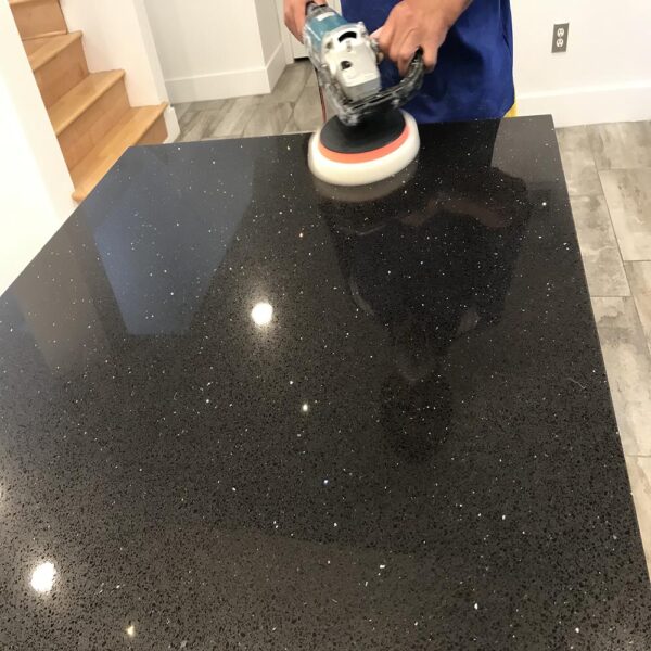 A person using a polishing machine to restore the shine of a black granite countertop.