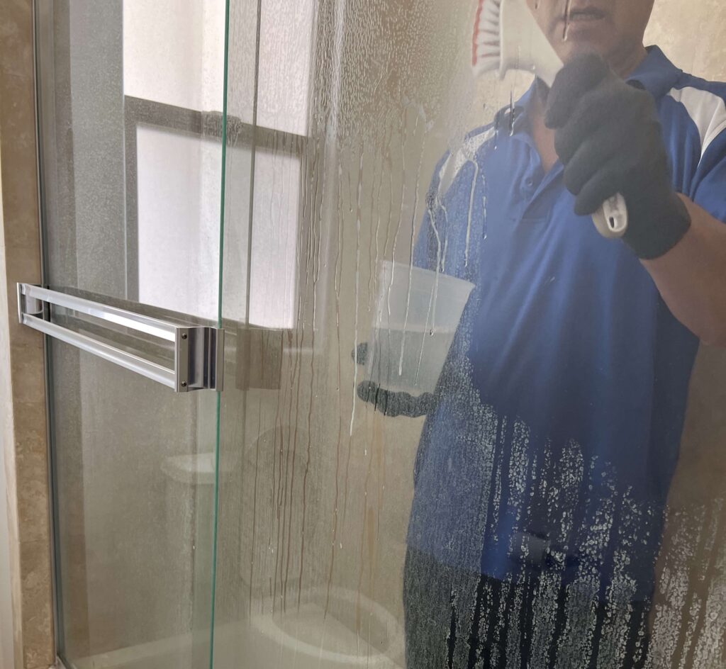 A professional cleaner in Torrance scrubbing a shower to remove soap scum and buildup.