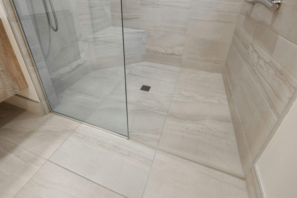 A modern tiled shower in Torrance, CA, with clean, light-colored tiles and sealed grout lines, featuring a glass door and a central drain.