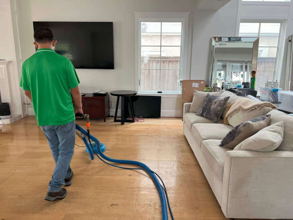 A professional technician using advanced water extraction equipment to clean and dry hardwood floors in a home affected by water damage.