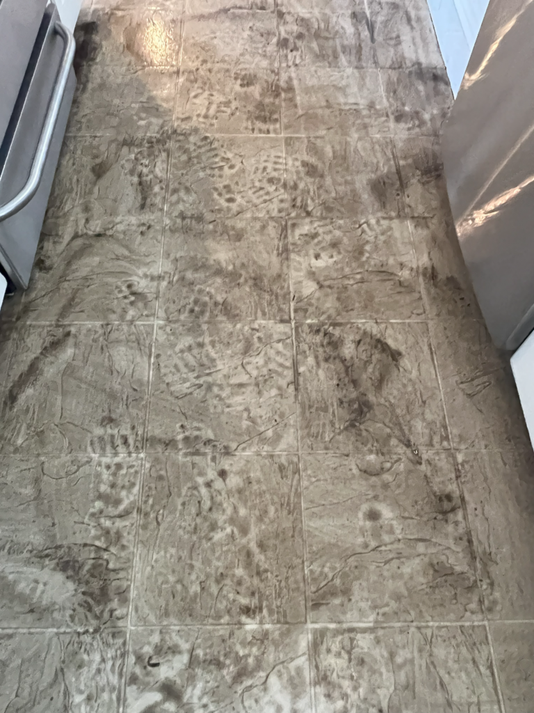 Dirty and stained tile flooring in an apartment kitchen, showing water damage and heavy soiling before the restoration process.