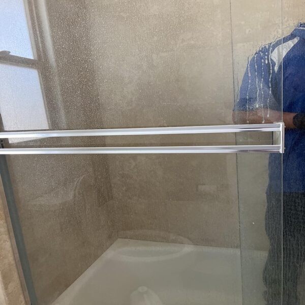 Close-up of hard water stains and mold residue on a shower glass door in a San Pedro bathroom